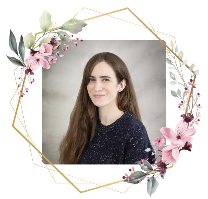 A picture of Grace Lee. She has long brown hair and green eyes. She is wearing a blue sweater in front of a gray background. She smiles at the camera. There is a gold border with pink flowers and green leaves around the photo.